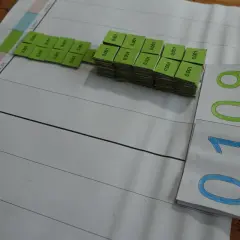Zestaw zielonych kostek z napisem "0,001" obok planszy z podziałką. Obok leżą karty z liczbami "0,109" i "0,1". To pomoc dydaktyczna do nauki ułamków dziesiętnych.